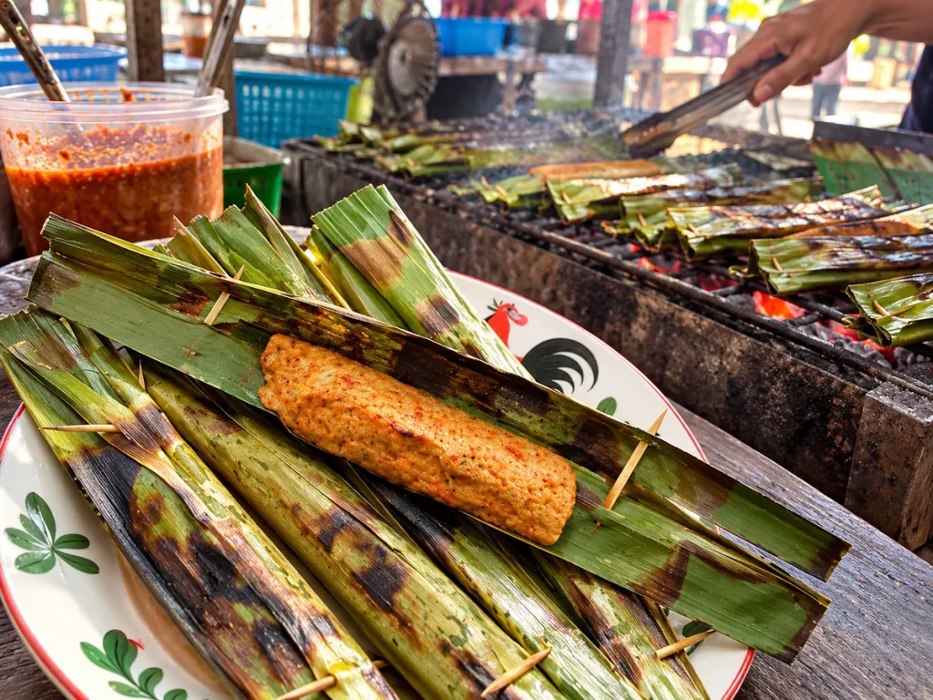 Otak-otak panggang berbungkus daun dengan latar lapak jajanan pasar makanan kuliner khas tanjung pinang